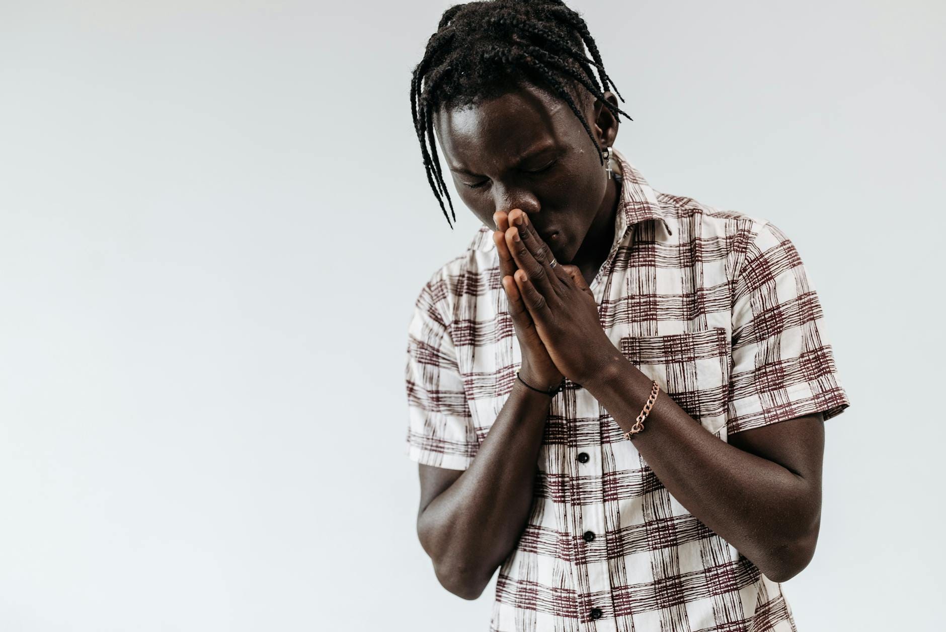 Młody mężczyzna w kratce modli się, składając dłonie na białym tle