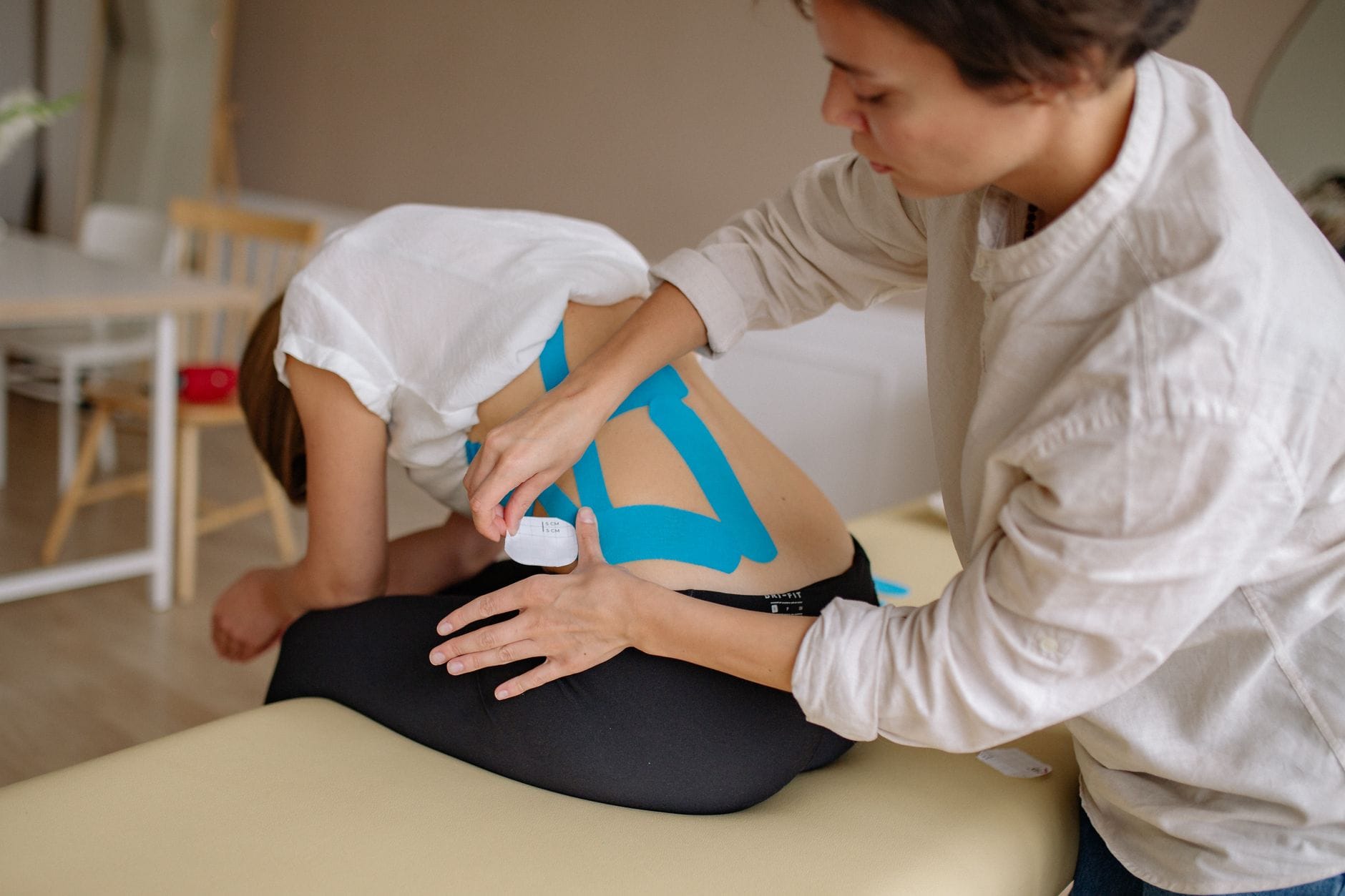 Fizjoterapeuta nakleja niebieskie plastry kinezjologiczne na plecy pacjenta
